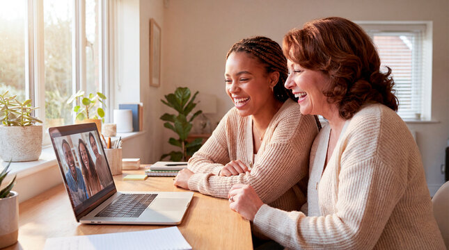 Two women laughing together during video call on laptop at bright home table