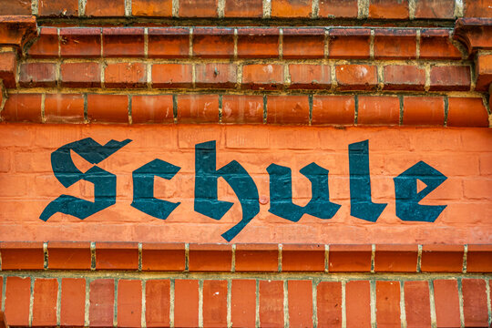 Old building with brick wall and the word Schule on the sign during daytime in a historical area - translation: school