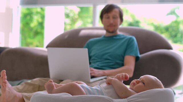 Working father on sofa with active baby in foreground. Slow motion.