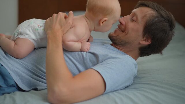 Smiling father cuddling two month old baby son on bed.