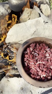 Rustic camping meal preparation with a terracotta pot simmering on a campfire.
