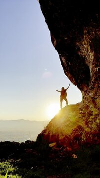 Silhouette of a man on a cave cliff spreading his arms and turning around to watch the sunrise