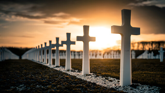 Rows of stone grave markers standing in a military burial ground during a sunset with golden light reflecting over the horizon while rows of monuments honor fallen soldiers in this peaceful