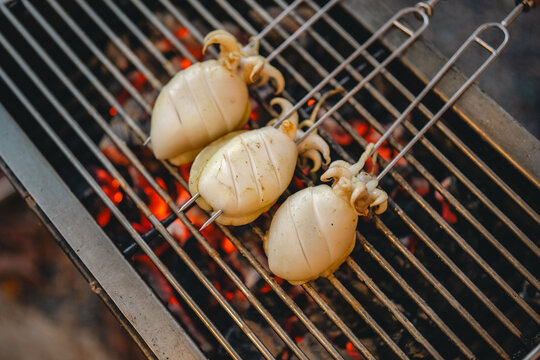 Grilled squid skewer barbecue seafood charcoal grill flame grate outdoor cooking with fresh cuttlefish roasting over hot ember for street food meal preparation
