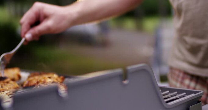 Close up of hand using metal fork to turn meat steaks cooking on hot outdoor barbecue charcoal grill