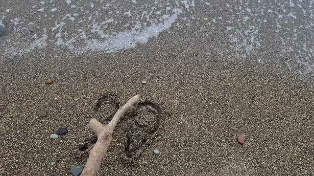Beach sand 2020 written with a wooden stick on the shoreline as the ocean tide gently rolls in during the day