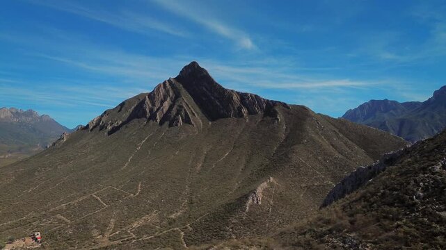 Aerial drone footage advancing forward toward Pico Morteros peak with serene blue sky and rocky mountain formations, capturing the monumental scale of the natural landmark in the Huasteca