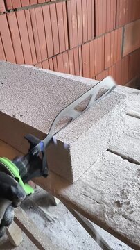 Cordless electric reciprocating saw cutting an aerated concrete block (AAC block). Construction tool in action during masonry work with close-up view of the cutting process.