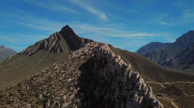 Aerial drone footage advancing forward toward Pico Morteros peak with serene blue sky and rocky mountain formations, capturing the monumental scale of the natural landmark in the Huasteca