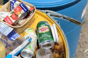 Obraz premium discarded food wrappers and drink containers, including Canada Dry, a carbonated beverage on a metal drum painted yellow in Toronto