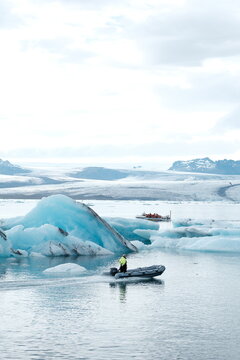 View of a zodiac boat navigating through the blue icebergs of Jokulsarlon Glacier Lagoon with snow-capped mountains in the background, Sveitarfelagid Hornafjordur, Iceland.
