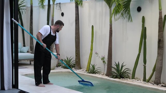 Poolman cleaning swimming pool with skimmer net at modern tropical villa. Professional pool maintenance video featuring routine cleaning, outdoor home care and property upkeep.