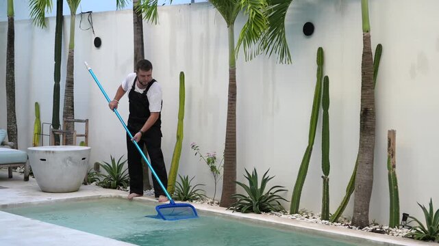 Poolman cleaning swimming pool with skimmer net at modern tropical villa. Professional pool maintenance video showing routine cleaning and outdoor property care.