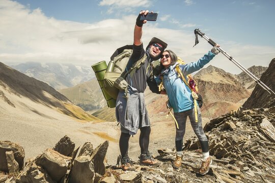 Happy couple of hikers taking selfie portrait on the top of the mountain - Smiling tourists enjoying summer day out - Boyfriend and girlfriend having