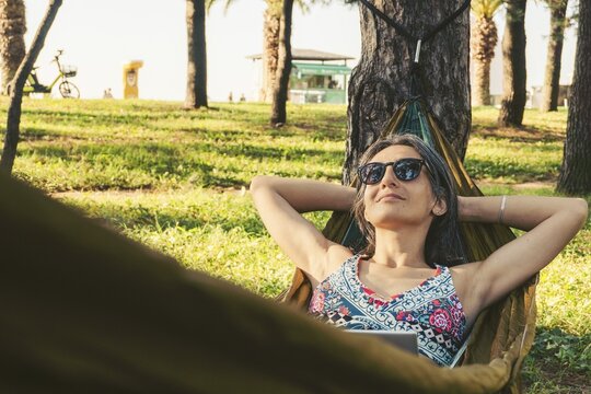Happy Young brunette caucasian woman in hammock relax browse net work enjoy nap in park on black sea coastline on remote working holiday vacation in caucasus. Blogger travel influencer digital nomad