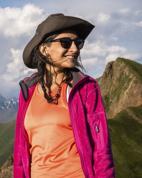 Happy Young Traveler hiker woman portrait wearing hat and jacket smiling in Kazbegi National Park mountains of Georgia, adventure lifestyle and hiking portrait