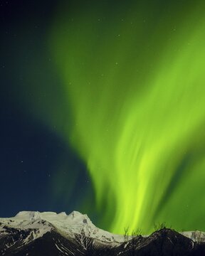 Brilliant green aurora borealis glowing above snowy mountain peaks under starry night sky, symbol of wilderness, beauty and protected national parks worldwide