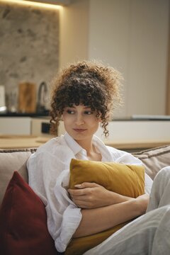Cozy moment at home for a young woman with curls holding a pillow in a modern living space
