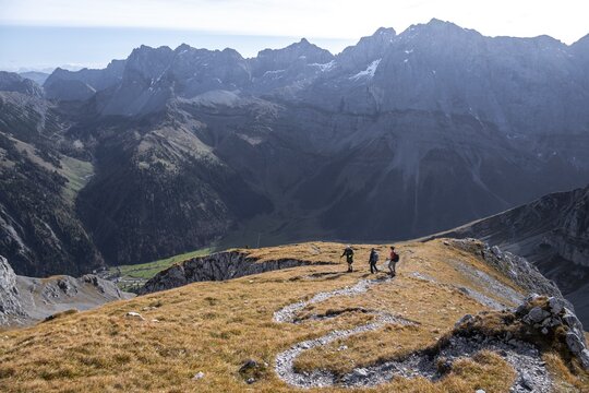 Three hikers descending, hiking trail with serpentines from Gamsjoch, dramatic rock faces of Hochgl&uuml;ck in the back, eastern Karwendel, Tyrol, Austria