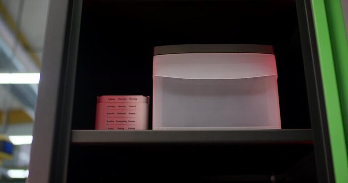 Close up view of a plastic container box and a roll of labels sitting inside an industrial metal cabinet