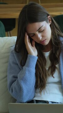Overworked young woman feeling tired and stressed while working on her laptop from home, suffering from a headache and eyestrain due to excessive screen time and professional burnout