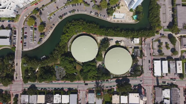 Top down aerial view of circular water storage tanks beside a winding canal in city area