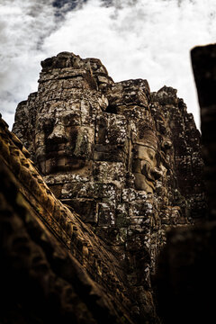 View of the iconic stone face carvings of Bayon Temple with weathered sandstone textures under a cloudy sky in Krong Siem Reap, Siem Reap Province, Cambodia.