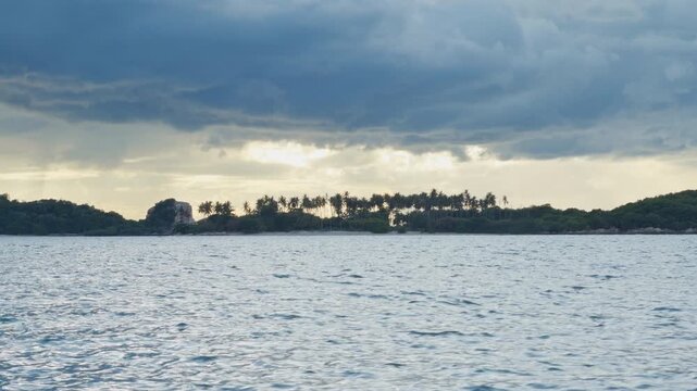 Slow Motion View of a Tropical Island Across Calm Water Beneath Dramatic Storm Clouds, Palm Trees, Rainfall, Coastal Scenery and Untamed Nature