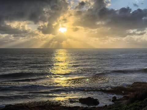 View of Cottesloe Beach at sunset with golden light reflecting on the ocean waves and dramatic clouds in the sky, Western Australia, Australia.