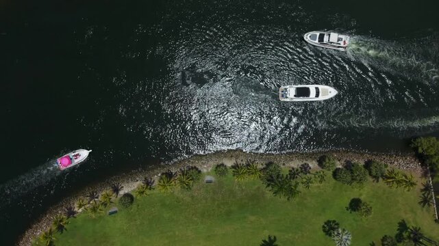 Top down aerial view of yachts cruising near a green waterfront park