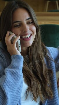Beautiful smiling woman with long brown hair having a pleasant conversation on her smartphone, laughing and enjoying the moment while relaxing on a comfortable sofa at home