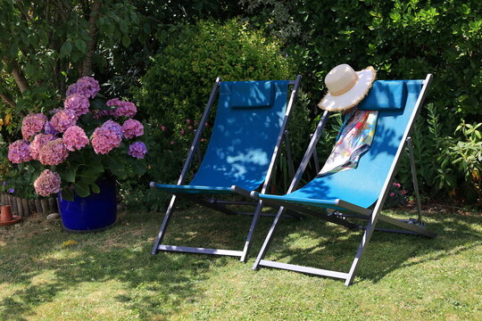 Transats in the summer garden. Relaxation spots bathed in sunlight amidst blooming flowers