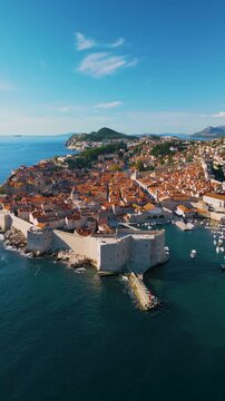 Epic Dubrovnik old town ancient castle architecture vertical aerial panorama. 
Cinematic drone panning flight of medieval stone fortress walls, 
terracotta roof tiles and blue Adriatic sea coast in Cr