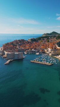 Epic Dubrovnik old town ancient castle architecture vertical aerial panorama. 
Cinematic drone panning flight of medieval stone fortress walls, 
terracotta roof tiles and blue Adriatic sea coast in Cr