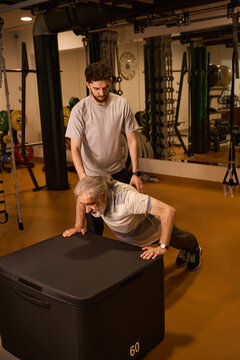 Elderly man performing push-ups with assistance in gym