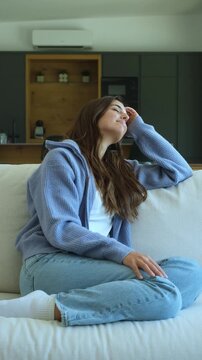 Beautiful happy woman sitting on a comfortable couch at home, smiling and enjoying a peaceful moment while daydreaming and looking out the window with sunlight on her face