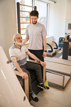 Elder male receiving assistance from adult male in therapy center