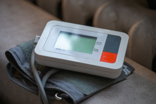 A portable digital blood pressure monitor rests on top of its folded grey arm cuff on a textured surface, ready for home health monitoring.