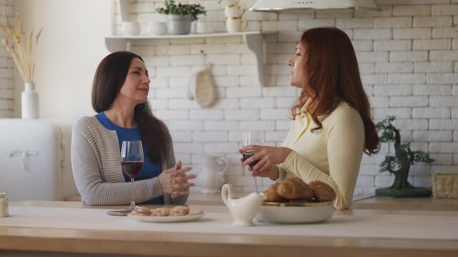 Joyful women in their 40s drinking wine and chatting at home, true friendship