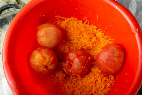 Top view of whole peeled tomatoes and grated carrots mixed in a bright red plastic bowl prepared for cooking