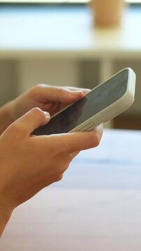 Detailed close-up shot of female hands holding a mobile phone and using thumbs to type a message, scroll through social media, or browse the internet, with a soft-focus background