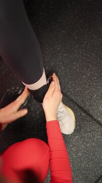 Vertical screen Personal trainer fastens an ankle strap for the client before cable kickbacks preparing for an effective glute workout with proper gym equipment setup