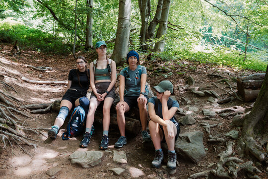 Group of Four Female Hikers Sitting on a Log to Take a Rest Break on a Rocky Forest Trail During a Summer Trekking Trip