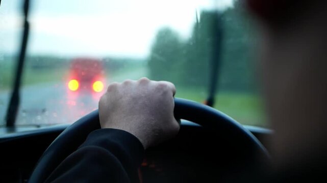 A close-up of a person's hand on the steering wheel while driving on a rainy road. Video for topics to transportation, travel, driving, trips, automobiles, safety, or navigation