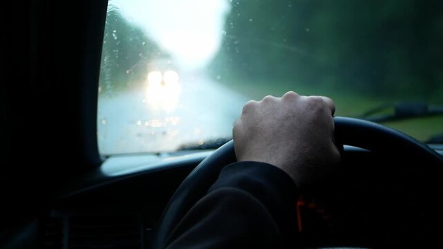 A close-up of a person's hand on the steering wheel while driving on a rainy road. Video for topics to transportation, travel, driving, trips, automobiles, safety, or navigation