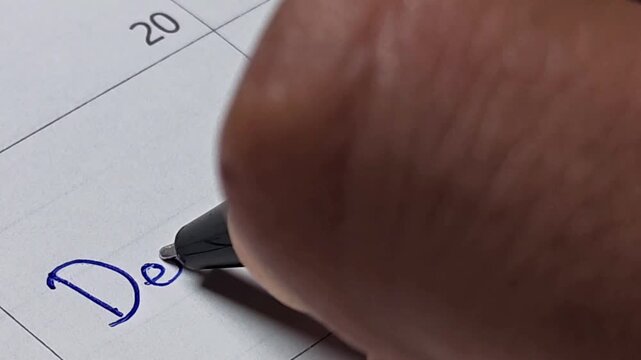 Close up of hand writing the word 'Dentist' with a blue pen on a paper calendar
