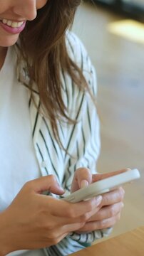 Close up view of an attractive young woman texting on her smartphone, smiling as she types and browses through her social media feed, enjoying her leisure time indoors at a table