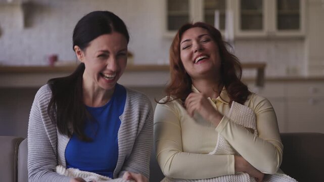 Cheerful middle-aged women friends laughing while watching a comedy show at home