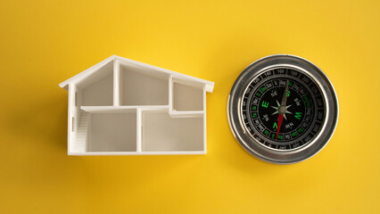 Top down view of an open white miniature house architectural floor plan next to a classic magnetic compass isolated on a yellow background. © MohamadFaizal