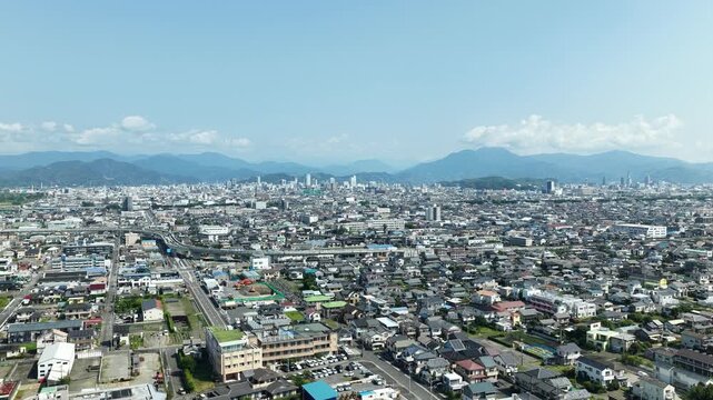 Aerial drone footage rising over Shizuoka city skyline with mountain backdrop in summer